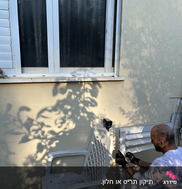 אדם מתקין תריסים ליד חלון עם תריסים לבנים